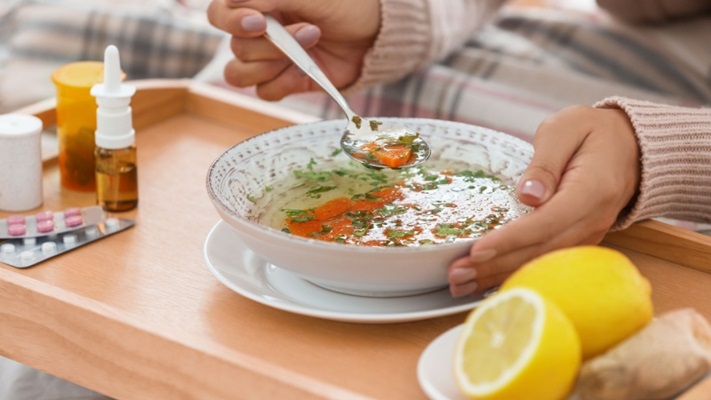 Mani mangiano minestrina accanto medicine limone e zenzero.